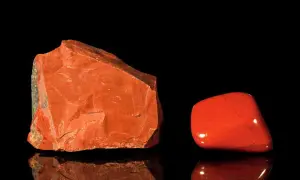 Zwei rote Jaspissteine, roh und poliert, spiegeln sich auf schwarzem Grund. Die imperial jaspis wirkung soll Kraft und Vitalität verleihen.