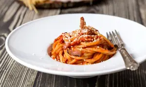 Un piatto di bucatini all'amatriciana, con guanciale croccante e una salsa rossa, spolverata di pecorino. La ricetta originale amatriciana cipolla, un classico intramontabile.