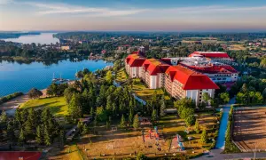 Hotel Gołębiewski w Mikołajkach, z czerwonymi dachami, otoczony zielenią i jeziorem, zaprasza na wypoczynek. Ile lat ma hotel? To miejsce z historią!