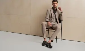 Elegancki mężczyzna w beżowym garniturze i kamizelce, siedzący na krześle. Na nogach ma stylowe loafersy, co to za buty, które dodają mu szyku.