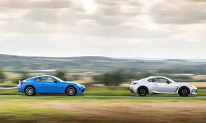 Dwa sportowe samochody, niebieska i srebrna Toyota 86, pędzą po wiejskiej drodze, tworząc dynamiczny obraz.