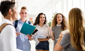 Uczniowie rozmawiają na korytarzu, trzymając książki. Czy na studium trzeba mieć maturę? To pytanie nurtuje wielu młodych ludzi.
