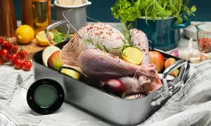 En rå kalkon i ugnsform med citron, lök och äpple. En digital termometer ligger redo för att mäta innertemp kalkon.