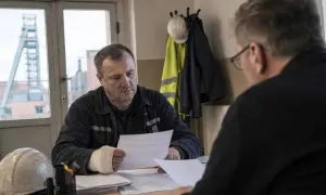 Górnik z opatrzoną ręką omawia dokumenty. Wypadek przy pracy to każde zdarzenie, które może się wydarzyć w miejscu pracy.