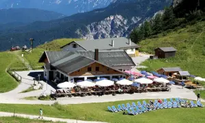 Die Hochalm Garmisch, ein beliebter Rastplatz mit vielen Gästen unter Sonnenschirmen, liegt malerisch vor einer beeindruckenden Bergkulisse.