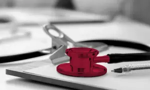 Un stéthoscope rouge vif sur un presse-papiers, prêt pour une visite médicale. Un stylo et une pince complètent la scène.