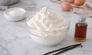 Un bol de crème chantilly aérienne, prêt à être dégusté. À côté, des gousses de vanille et une petite bouteille d'extrait.