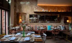 Gemütliches Restaurant mit Ziegelwänden und Tischen, gedeckt für Gäste. Eine leuchtende Neon-Schrift "More Light" hängt über dem Sitzbereich.
