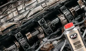 Widok wnętrza silnika z widocznymi wałkami rozrządu i olejem. Obok butelka preparatu K2 Motor Flush do płukania silnika.