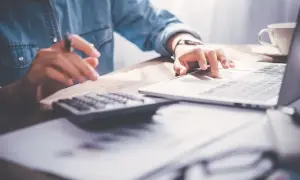 Person rechnet am Laptop und mit Taschenrechner. So lassen sich Maklerkosten absetzen.
