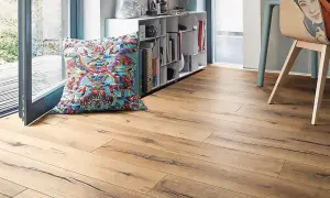 Un suelo laminado de madera clara con un cojín colorido y una estantería llena de libros.