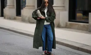 Stylische Frau in dunkelgrünem Mantel und Barrel Jeans, die sie lässig kombiniert. Sie trägt eine weiße Rollkragenpullover und auffällige Schuhe.
