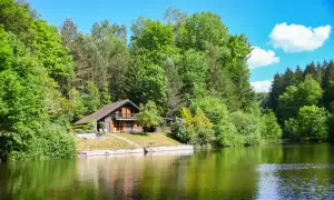 Charmant chalet en bois au bord d'un étang de pêche privé en Alsace, entouré de verdure luxuriante.