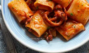 Paccheri con sugo di calamari, un piatto di mare saporito e colorato, con tentacoli che spuntano dalla pasta.