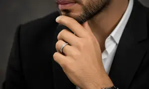 Un hombre con traje negro y camisa blanca luce un elegante anillo bulgari oro blanco y amarillo, adornado con diamantes.