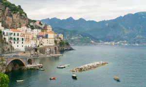 Malownicze miasteczko na klifie wzdłuż wybrzeża Amalfi, z łodziami na lazurowej wodzie i górami w tle.