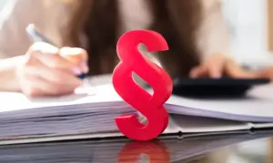 Czerwony symbol paragrafu na tle osoby pracującej z dokumentami i kalkulatorem symbolizuje różne rodzaje wykładni prawa.