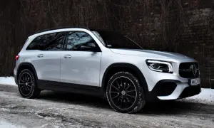 Srebrny Mercedes GLB 200 na zimowej drodze, z czarnymi felgami i przy ceglanym murze.