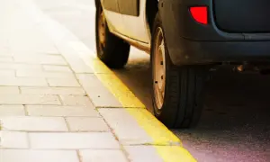 Un coche aparcado junto a una acera con marcas viales amarillas. El significado de estas marcas viales amarillas indica prohibición de estacionar.