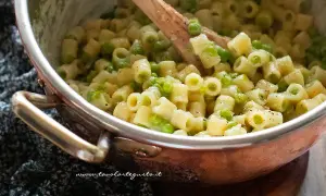 Un primo piatto cremoso di pasta e piselli, mescolata con un cucchiaio di legno in una pentola di rame.