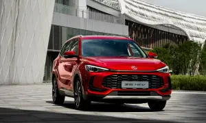 Czerwony MG ZS HEV, nowoczesny SUV, zaparkowany przed futurystycznym budynkiem.