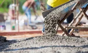 Beton na fundament wylewany z rynny. Pracownicy w tle budują solidną konstrukcję.
