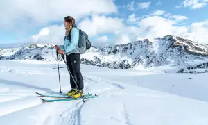 Frau mit Rucksack und Skitourenausrüstung in verschneiter Berglandschaft. Perfekte Packliste Skitour für Abenteuer.