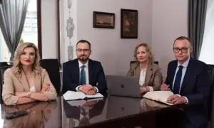 Cztery osoby w strojach biznesowych siedzą przy stole w sali konferencyjnej, przed nimi dokumenty i laptop.