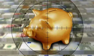 Un salvadanaio dorato è nel mirino, circondato da pile di banconote. Un'immagine che evoca la fragilità del risparmio, un **unit linked** da proteggere.