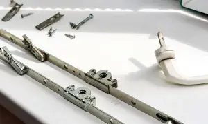 Zepsuta klamka w oknie plastikowym. Rozłożone mechanizmy i śruby czekają na naprawę.