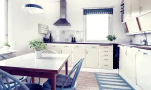 Ett ljust kök med charmigt funkishus från 40-talet. Ljusblå stolar runt ett vitt bord, beige skåp och en blommig fönstergardin.