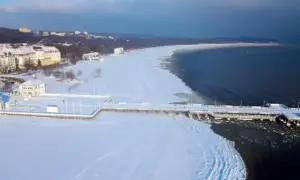 Zimowe atrakcje pomorskie: molo w Sopocie otoczone lodem i śniegiem, z widokiem na zamarznięte morze i nadmorskie budynki.