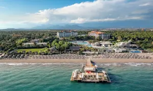 Turkusowe morze w Turcji otacza luksusowy kurort z molo, basenami i plażą pełną leżaków.