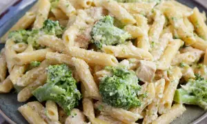 Penne z kurczakiem i kremowym sosem, w którym dominują zielone różyczki brokułów. Danie posypane startym parmezanem.