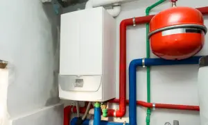 Montaż kotła gazowego w toku. Biały kocioł, czerwony zasobnik i kolorowe rury tworzą instalację grzewczą.