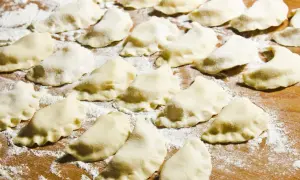 Surowe pierogi ułożone na drewnianej desce, posypane mąką.