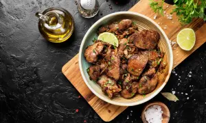 Un piatto invitante di fegatini di pollo con patate, guarnito con spicchi di lime e prezzemolo fresco. Accanto, olio d'oliva, sale grosso e pepe.