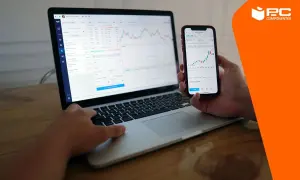Persona usando un portátil y un móvil para conectar movil a pc y ver gráficos financieros.