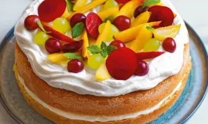Torta compleanno pan di spagna con panna montata e frutta fresca: pesche, uva rossa e bianca, prugne e foglioline di menta.
