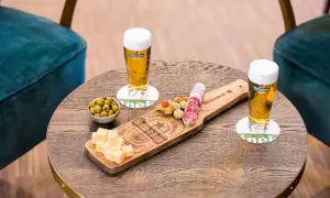 Due bicchieri di birra ale Heineken con salumi, formaggio e olive su un tavolino di legno.