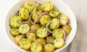 En skål med fransk potatissallad, full av små, kokta potatisar, rödlök och färsk persilja.