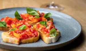 Bruschetta mit Tomaten und Basilikum auf einem grauen Teller.
