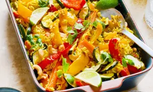 Reisgericht mit buntem Gemüse, Cashewkernen und Limettenspalten in einer Auflaufform.