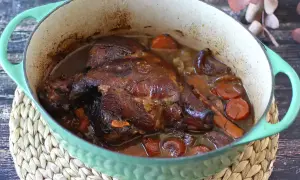 Un gigot de 7 heures mijoté dans une cocotte verte, avec des carottes et des oignons. La viande est tendre et dorée, prête à être dégustée.