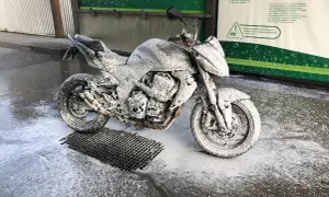 Motocykl pokryty pianą na myjni. Widać instrukcję, jak myć motocykl, z zaleceniem zachowania bezpiecznej odległości.