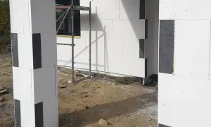 Budowa domu z bloczków styropianowych. Zastanawiasz się, czym przykleić styropian do blachy? Tutaj widzisz fragmenty ścian i słupa z białego styropianu z czarnymi wstawkami.