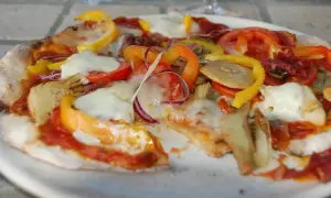 En pizza med surdegsbotten, toppad med mozzarella, paprika, tomat, rödlök och kronärtskocka.