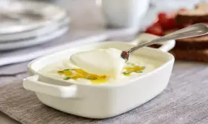 En sked lyfter krämig bechamelsås ur en vit skål, perfekt för ditt bechamelsås recept.