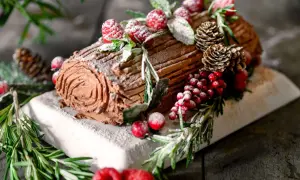 Ein köstliches Bûche de Noël Rezept Original: Schokoladenrolle mit Beeren, Tannenzapfen und Rosmarin, bestäubt mit Puderzucker.