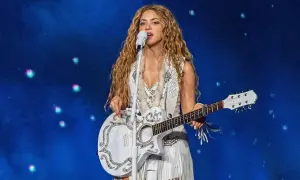 Shakira śpiewa i gra na gitarze podczas koncertu w Polsce. Wokalistka ma długie, falowane włosy i biały, zdobiony strój.